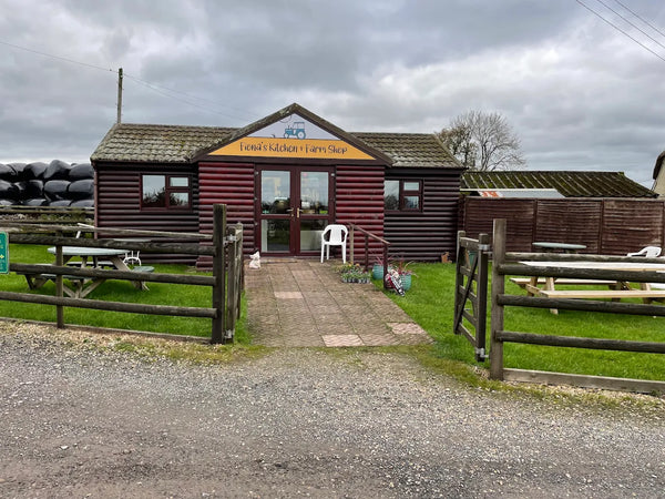 Wooden building with a sign on a cloudy day, surrounded by greenery and picnic tables.