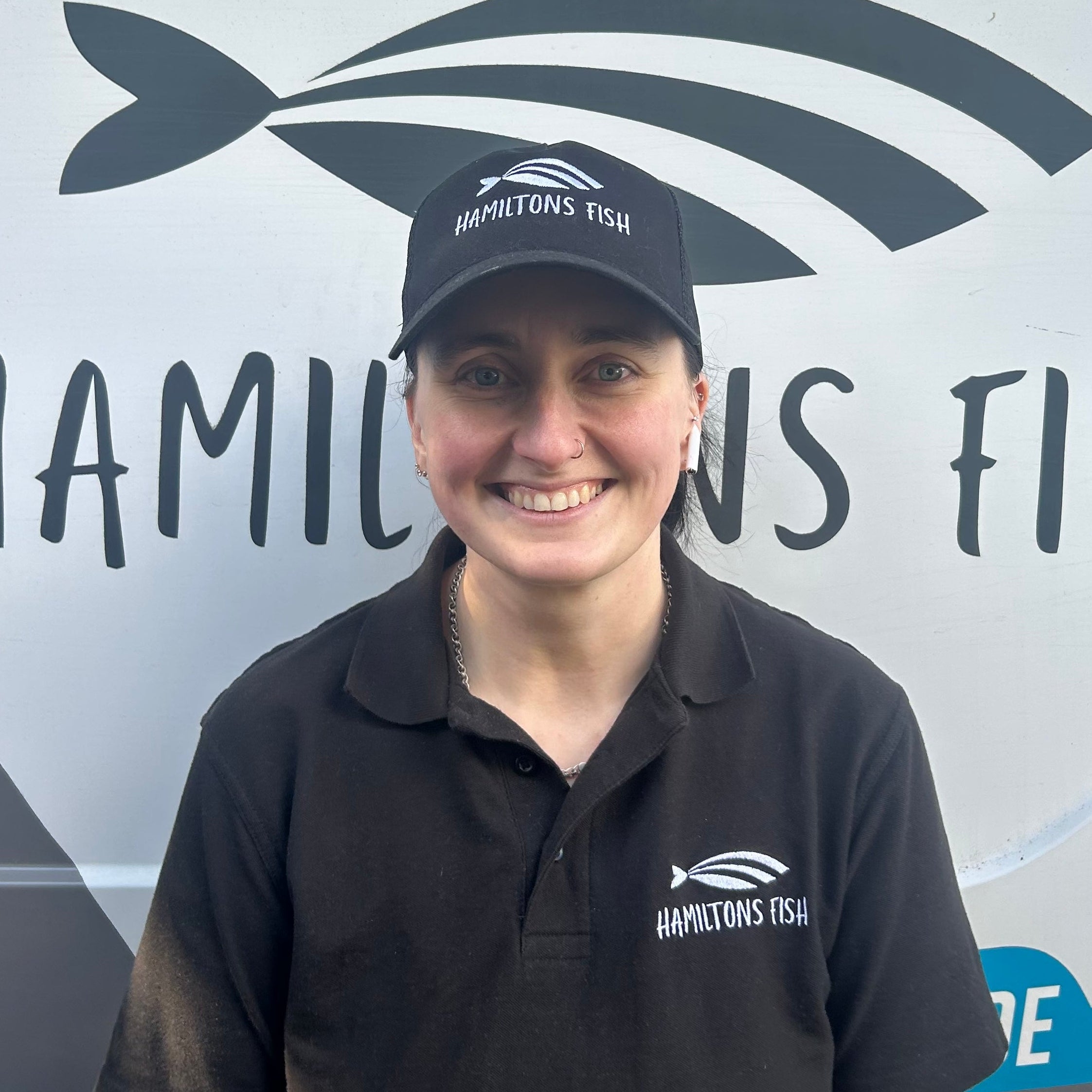 Laura Hamilton wearing a black cap and polo shirt with Hamiltons Fish logo in front of a branded background.
