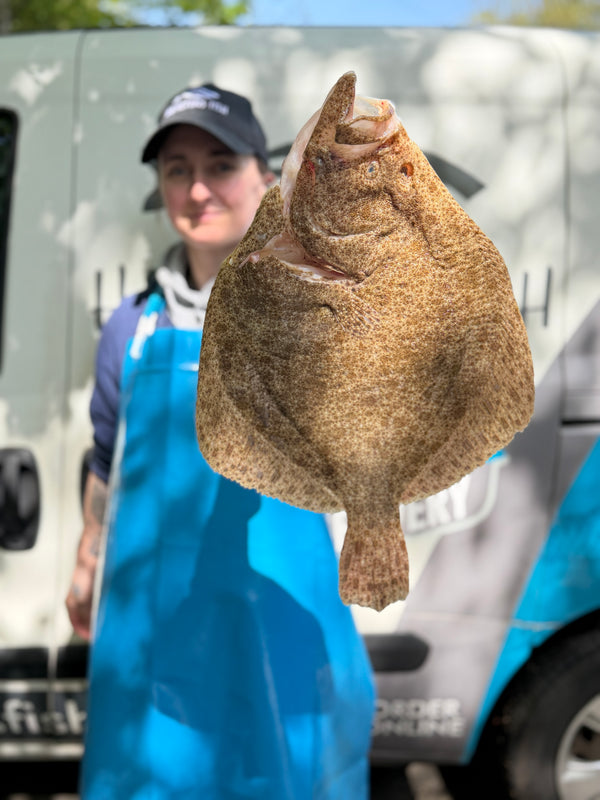 Person holding a large turbot in front of a vehicle