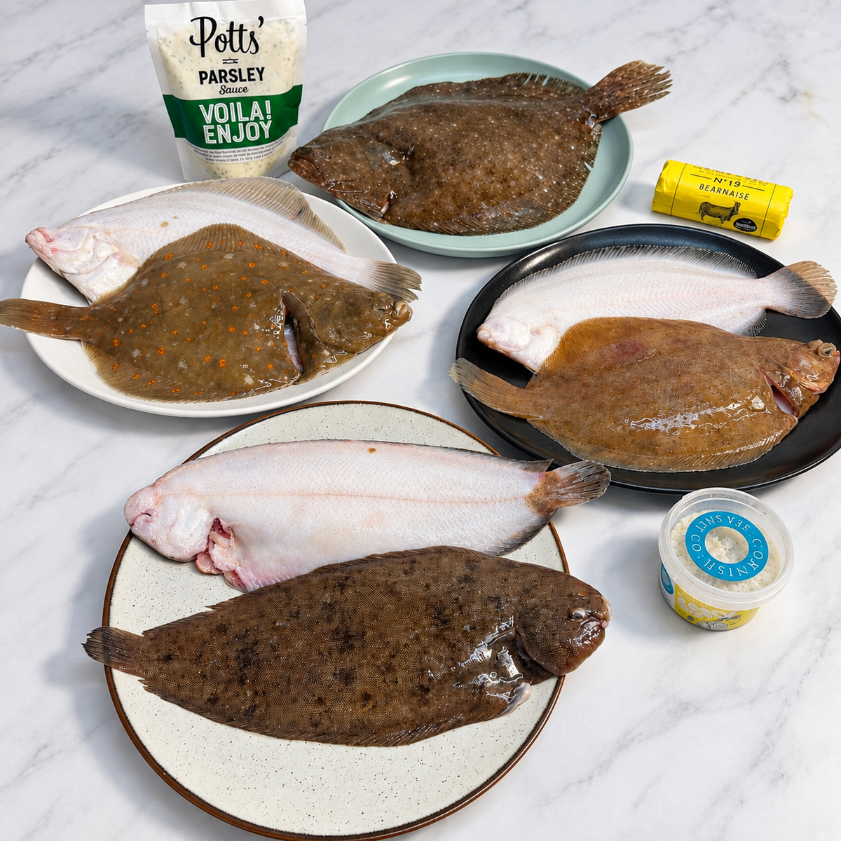 Sevon whole flatfish arranged on plates with Potts' Parsley sauce! Plus seasoning and butter on a white marble surface.